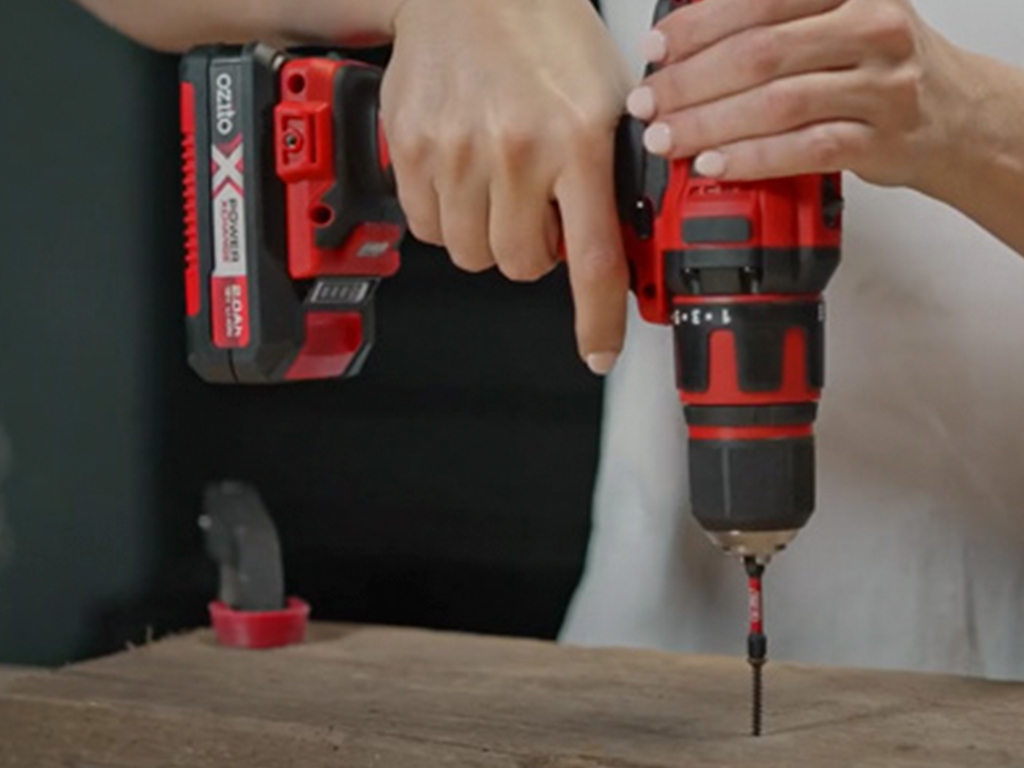 A woman is screwing a screw into wood with a cordless screwdriver