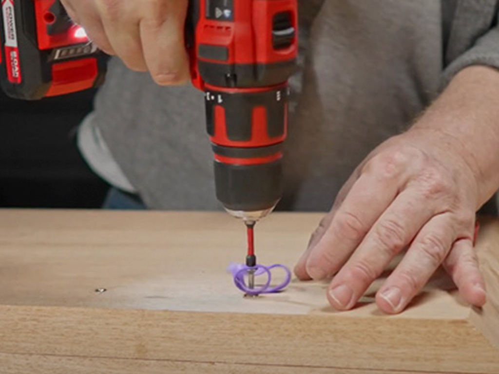 A woman is screwing a screw into wood with a cordless screwdriver