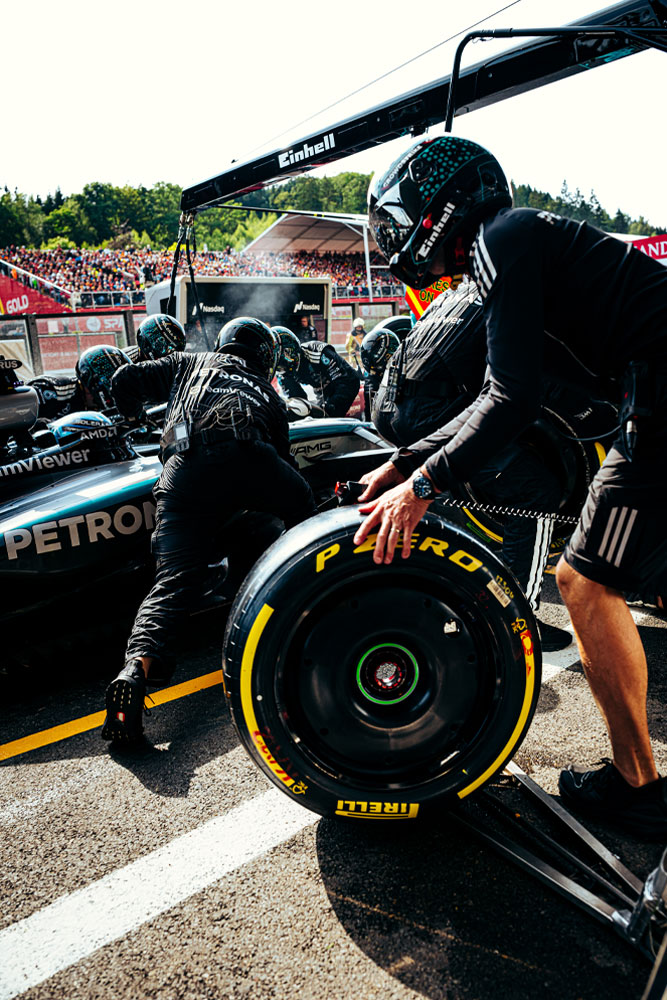 Mercedes-AMG PETRONAS Formula One Team mechanics are performing a pit stop. One crew member is preparing a Pirelli tire while others work on the car. Einhell branding is visible on the equipment above the car.